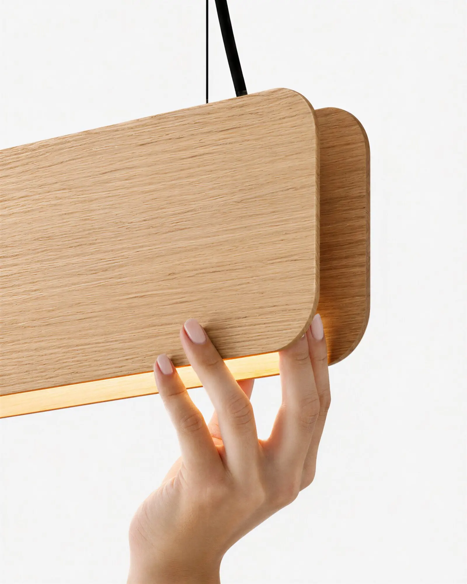 nina-japandi-linear-oak-suspension-lamp Close-up detail of the Nina linear pendant light by Singular Lighting, featuring natural oak wood panels, black suspension cables, and a warm LED glow, gently held by a hand.