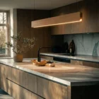 Singular Lighting - NINA Pendant P120-01 Sleek linear oak wood suspension luminaire glowing above a dark marble kitchen island in a luxury home