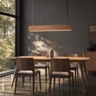 Singular Lighting - NINA Pendant P120-06B A sleek natural oak pendant light (the 'Nina' lamp) hanging above a modern wooden dining table and grey-upholstered chairs. Sunlight from a large window creates intricate shadow patterns on the wall