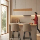 Singular Lighting - NINA Pendant P120-10B A natural oak pendant light (the 'Nina' lamp) illuminating a light wood kitchen counter with two upholstered bar stools.