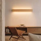 Nina Wall linear wooden up-and-down lamp by Singular Lighting, in a minimal living room above an oak console with a leather chair. Warm ambient light, natural oak finish.