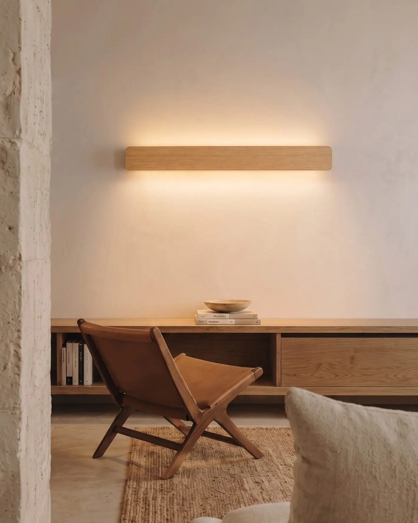 Nina Wall linear wooden up-and-down lamp by Singular Lighting, in a minimal living room above an oak console with a leather chair. Warm ambient light, natural oak finish.