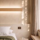 nina-wall-oak-linear-up-down-lighting-bedside Bedside Nina Wall linear oak up-and-down light by Singular Lighting, next to a dimmer switch on a textured wall. Minimalist bedroom nightstand with a glass of water.