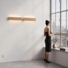 nina-wall-oak-linear-up-down-lighting-city-view-apartment A woman in a black dress overlooking a city skyline from a modern apartment, illuminated by two linear natural oak Nina Wall lights by Singular Lighting. High-rise view.