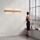 A woman in a black dress overlooking a city skyline from a modern apartment, illuminated by two linear natural oak Nina Wall lights by Singular Lighting. High-rise view.